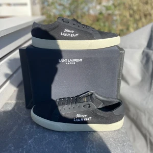 Svarta sneakers från Saint Laurent - Snygga svarta sneakers från Saint Laurent med vit sula och märkets logga på sidan. Perfekta för en stilren look. Skorna har snörning och en rund tå.