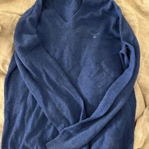 Blå tröja från GANT - Säljer en stilren blå tröja från GANT med v-ringning. Tröjan har långa ärmar och är perfekt för kyligare dagar. Den är tillverkad i ett mjukt material som ger en bekväm passform.