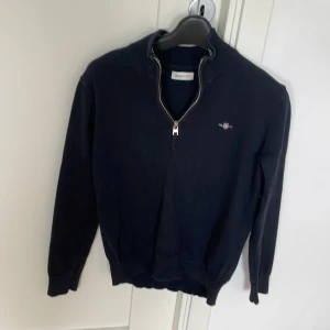 Marinblå halv zip från Gant - Snygg svart tröja från Gant med dragkedja vid halsen. Perfekt för en stilren look. Tröjan har långa ärmar och en liten logga på bröstet. 