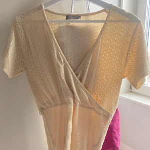 Beige omlottopp - Snygg beige omlottopp med korta ärmar och ribbad struktur. Perfekt för en stilren look. Passar bra till både jeans och kjol.