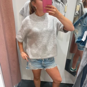 Grå stickad tröja - Säljer en stilren grå stickad tröja med korta ärmar. Perfekt för en avslappnad look. Tröjan har en rund halsringning och en mjuk känsla. Passar bra till jeans eller kjol.