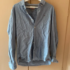 Blå skjorta från Hilfiger Denim - Säljer en stilren blå skjorta från Hilfiger Denim. Skjortan har en klassisk krage och knappar framtill. Skjortan är i regular fit