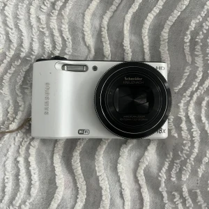 Samsung digitalkamera - Säljer en Samsung-kamera i bra skick, modell WB150F. Observera att laddare och minneskort inte ingår, men batteriet följer med. Kameran kan enkelt laddas med en vanlig Samsung-laddare. Dessutom har den Bluetooth-funktion, vilket gör det möjligt att överföra bilder direkt till din Samsung-enhet. Tveka inte att höra av dig om du har några frågor eller funderingar! 😊