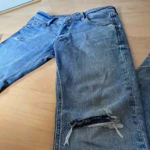 Blå jeans med slitningar - Säljer ett par blå jeans från Jack&Jones, modellen heter Slim Glenn och har en riktigt snygg Slim passform ända ner till fötterna. Slitningarna är från fabrik! Skriv gärna till oss vid frågor! W28/29 L32