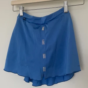 Blå kjol från Passionice - Snygg blå kjol från Passionice med glittriga kristaller framtill. Den är i storlek 142 och har innertrosa. Går ej att köpa från hemsida! Har ni några frågor är det bara att ställa! 💕