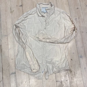 Beige långärmad skjorta från 157 - Säljer en beige långärmad skjorta från 157 i storlek M. Skjortan har klassisk krage, knappar hela vägen och är gjord i mjuk bomull. Perfekt för dig som gillar enkel och clean stil. Passar dig som vill ha en neutral färg i garderoben.