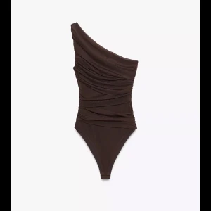 Brun one shoulder topp i mesh - Säljer en brun, tight och transparent one shoulder topp i mesh med draperade detaljer. Toppen är figurnära och har en asymmetrisk axel, vilket ger en snygg och modern look. Perfekt att styla med jeans eller kjol för en trendig outfit.