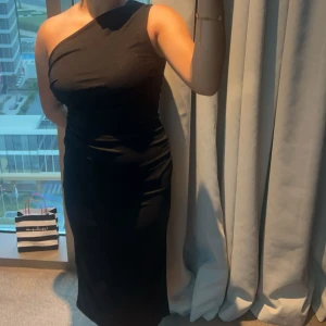 Svart oneshoulder långklänning - Säljer en svart långklänning med oneshoulder-design som ger en snygg och modern look. Klänningen har en tight passform och är tillverkad i ett mjukt material som sitter bekvämt mot kroppen. Perfekt för dig som vill sticka ut med en stilren och elegant outfit.