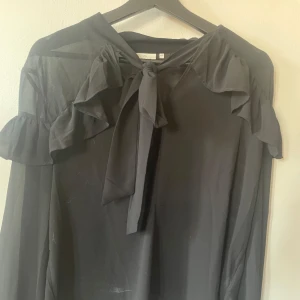 Svart genomskinlig blus - Svart genomskinlig blus från KAFFE. Fina volanger på axlarna och knyte framtill. Storlek 42. 30kr+frakt