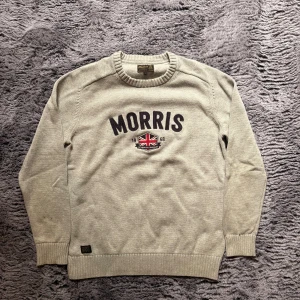 Grå stickad tröja från Morris - L passar s/m Snygg stickad tröja från Morris med broderad logga och brittisk flagga framtill. Tröjan har rund halsringning, ribbade muddar och är långärmad. Perfekt för dig som gillar klassisk och stilren look.