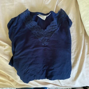 Mörkblå långärmad topp med spets - Mörkblå långärmad topp från Gina Tricot med snygg v-ringning och dekorativ spetsdetalj längs halsringningen. Mjuk och skön bomullskänsla, perfekt för dig som gillar stilrena plagg med en twist.