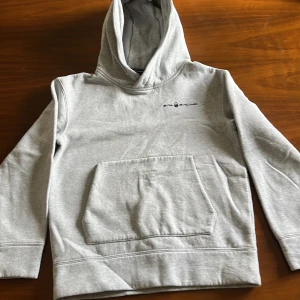 Grå hoodie från Sail Racing - Snygg ljusgrå hoodie från Sail Racing med svart logga på bröstet. Klassisk känguruficka framtill och stor huva. Mjuk insida och långärmad modell, perfekt för chill dagar. Passar dig som gillar enkel och stilren streetwear. Nypris: 1100 mitt pris: 500