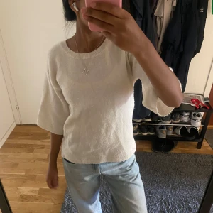 Vit stickad topp med trekvartsärm - Mysig vit stickad topp med rund halsringning och trekvartsärmar. Perfekt för dig som gillar en enkel och clean stil. Passar till både jeans och kjol för en avslappnad look.