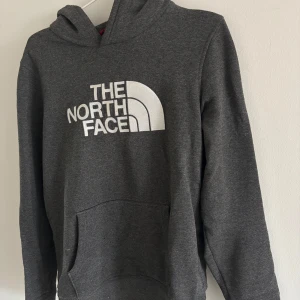 Mörkgrå hoodie från The North Face - Säljer en mörkgrå hoodie från The North Face med stor vit logga på bröstet. Använd ett fåtal gånger, kommer i mycket bra skick. 