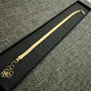 Guldigt armband med tunn kedja - Stilrent armband i guldton med tunn, platt kedja och justerbar längd. Låset är av klassisk karbinmodell och armbandet har flera öglor för perfekt passform. Perfekt accessoar för att lyfta din look. Helt nya oanvända Vid retur står köparen för Frakten/Returen. Jag ansvarar inte för postens slarv.