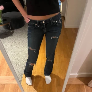 True Religion mörkblå bootcut jeans - Mörkblå jeans från True Religion med egnagjora hål. Låg midja och bootcut passform. Snygga bakfickor med lock och silverfärgade knappar. Köpte dom här på Plick! Dom första 2 bilderna är från hon jag köpte dom av o dom andra 2 är hur dom är på mig!!💞💞 Dom är i storlek 25/30!