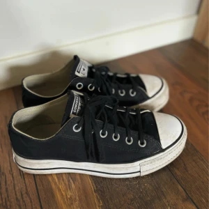 Svarta Converse All Star sneakers - Klassiska svarta Converse All Star sneakers med lågt skaft och vit sula. Skorna har snörning, rund tå och är tillverkade i canvas med detaljer i vitt och svart. Perfekta för en avslappnad och cool stil.