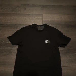 Svart Moncler t-shirt  - Svart t-shirt från Moncler i bomull med diskret logomärke på bröstet. Klassisk passform och rund halsringning, perfekt för en clean och stilren look. T-shirten har korta ärmar och känns riktigt lyxig med sin enkla design.storlek medium men passar S, tröjan köptes i london och har endast blivit använd runt 3-4 gånger, vid snabb affär kan priset diskuteras🙌vid  frågor och funderingar så är det bara att hojta till👍