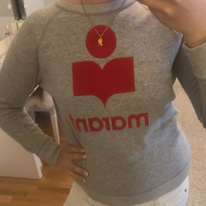 Grå sweatshirt från Isabel Marant - Säljer en grå sweatshirt från Isabel Marant Étoile med rött tryck och logga framtill. Tröjan har rund hals, långa ärmar och är tillverkad i mjuk bomull.  Verkligen en så snygg tröja 🩷