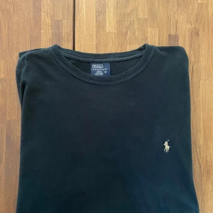 Svart t-shirt från Polo Ralph Lauren - Svart t-shirt från Polo Ralph Lauren med klassisk rund hals och korta ärmar. T-shirten har en liten broderad logga i vitt på bröstet och är gjord i mjuk 100% bomull. Enkel och stilren design som funkar till allt. Storleken är S enligt etiketten men skulle säga M då t shirten passar mig. T shirten har används någon gång bara. 