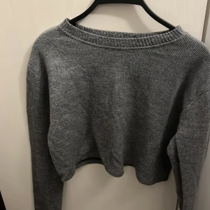 Grå ribbad stickad tröja från Zara - Mysig grå stickad tröja från Zara i ribbat material. Tröjan har en avslappnad passform, rund halsringning och långa ärmar. Perfekt för lager-på-lager och chill dagar. Enkel att matcha med jeans eller kjol.