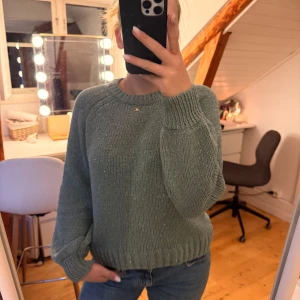 Grön glittrig stickad tröja H&M - Mysig grön stickad tröja från H&M med diskret glittrigt garn. Tröjan har rund halsringning, långa ärmar och ribbade muddar. Perfekt för dig som gillar en enkel men ändå lite extra look.