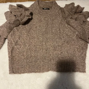 Beige stickad tröja med volangärmar - Superfin beige stickad tröja från Gina Tricot med högt ribbat halslinne och unika volangdetaljer på ärmarna. Kabelstickat mönster framtill och croppad passform. Perfekt för dig som vill ha något extra till höst och vinter.