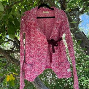 Odd Molly rosa kofta med mönster - Säljer en snygg rosa och vit kofta från Odd Molly med grafiskt mönster och lång ärm. Koftan har en cool omlott-design med mörkbrunt knytband i midjan och mjukt stickat material. Perfekt för dig som gillar färg och unika detaljer! Storlek 4 som enligt deras storleksguide motsvarar en storlek M/L. Den är liten i storlek. Fint skick, men den kan finnas ytludd och noppror. Material är ull och nylon. 