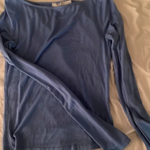 Blå långärmad topp från NA-KD - Säljer en enkel och stilren blå långärmad topp från NA-KD i storlek XS. Toppen har en rund halsringning och är gjord i ett mjukt, tunt material som känns skönt mot huden. Perfekt att styla med jeans eller kjol för en clean look.