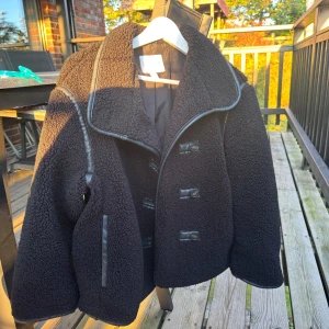 Svart teddyjacka med stora knappar - Säljer en svart teddyjacka med oversized passform och stora knappar framtill. Jackan har bred krage, detaljer i fejkskinn längs kanterna 