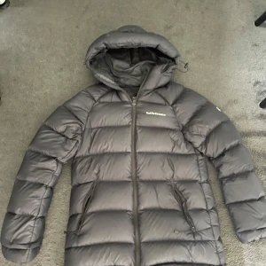 Svart dunjacka Peak Performance XS - Säljer en svart dunjacka från Peak Performance i storlek XS. Jackan är lång, har huva och dragkedja framtill samt två fickor med dragkedja. Perfekt för kalla dagar och riktigt skön att bära. Klassisk och stilren design med logga på bröstet.