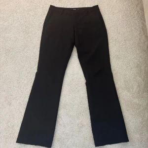 Svarta bootcut kostymbyxor BikBok - Snygga svarta kostymbyxor från BikBok i storlek 38. Byxorna har bootcut-ben, klassiska fickor och stängs med dragkedja och knapp. Perfekta för en clean och stilren look. Materialet känns mjukt och följsamt.