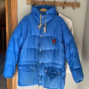 Blå dunjacka från Fjällräven - Säljer en blå dunjacka från Fjällräven med huva och gula dragsnören. Köpte den begagnad, finns lite fläckar men går nog bort med något mirakelmedel. Storlek 44-46, och jag har vanligtvis L -XL i jacka. Är 160 lång 