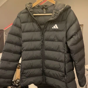 Svart Adidas jacka - Svart pufferjacka från Adidas med huva och dragkedja framtill.  Jackan är som ny och köptes för 900kr säljer pga av aldrig andvänds.
