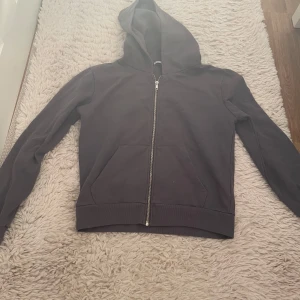 Blågrå hoodie med dragkedja från 157 - En svart hoodie från 157 i storlek S. Tröjan har huva, hel dragkedja framtill och två stora fickor. Tillverkad i mjuk bomullsmix med fleece på insidan, perfekt för kyliga dagar. Enkel och stilren design som funkar till det mesta.