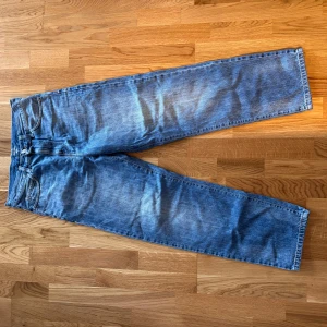 Blå jeans från Carhartt WIP - Säljer ett par klassiska blå jeans från Carhartt WIP med raka ben och normal passform. Jeansen har fem fickor, synliga sömmar och Carhartt-logga på bakfickan. Tillverkade i slitstarkt bomullsjeansmaterial. Byxorna är i mycket bra skick. Anledningen till att de säljs är att de ej längre kommer till användning. Modellen på byxorna heter Smith Pant och är i storlek 28.