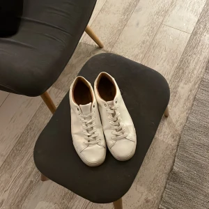 Vita minimalistiska sneakers i skinn - Snygga vita sneakers i minimalistisk design med rund tå och platt sula. Skorna har vita snören och diskreta sömmar, samt en ljusbrun insida. Perfekta för dig som gillar en clean och stilren look.