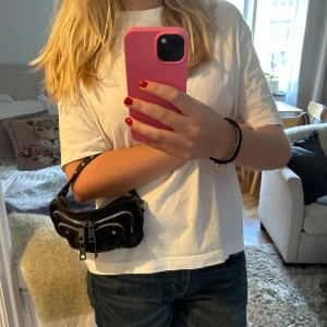 Svart axelväska med kedja från Nunoo - Cool svart axelväska i skinn från Nunoo med silverfärgad kedja som axelrem. Väskan har flera fack och detaljer med nitar på remmen. Perfekt storlek att använda som clutch! Väskan har inga defekter och är i nyskick! 