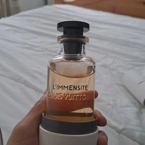 Louis Vuitton L'Immensité Eau de Parfum - Jag har kvittot Exklusiv parfym från Louis Vuitton, 'Immensité. Flaskan är i genomskinligt glas med svart lock och elegant tryck. Parfymen har en ljus bärnstensfärgad vätska. Kommer i original vit kartong och rund förvaringsask med stilren design.