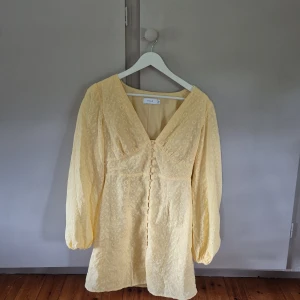 Gul kortklänning från Vila - Superfin gul kortklänning från Vila med broderade blommor, v-ringning och knappar framtill. Klänningen har långa puffärmar och smock i ryggen för en snygg passform. Storlek 36, skulle säga att den även passar er som är mellan storlek S-M. För er som är rädda att den blir för tight över bröstet så har jag 75D för referens. Använd någon enstaka gång, väldigt bra skick. 