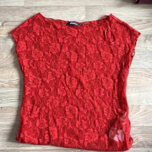 Röd spetsblus från Gina Tricot - Säljer en röd blus i genombruten spets från Gina Tricot. Blusen har ett blommigt spetsmönster med rosor och är ärmlös med rund halsringning. Perfekt för dig som vill sticka ut med en färgstark och romantisk look.