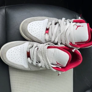Nike Air Jordan 1 Low Vit/Röd 42,5 - Nike Air Jordan 1 Low i vitt och rött med grå mockadetaljer. Klassisk röd swoosh och röd insida, perforerad tå och snörning. Skön platt sula och ikonisk Jordan-logga på plösen. Perfekta sneakers för dig som gillar streetstyle.
