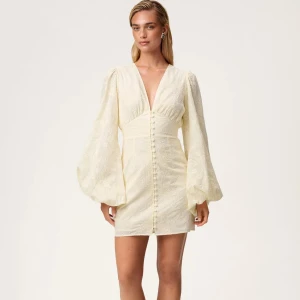 Ljus Adoore klänning med puffärmar - Superfin ljus kort klänning med djup v-ringning, puffiga långärmar och dekorativa knappar framtill. Klänningen har broderade detaljer i tyget och markerad midja för en snygg siluett. Perfekt för sommarens alla tillfällen! Kan diskutera till ett rimligt pris!