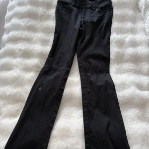 Svarta bootcut byxor från Monki - Svarta bootcut byxor från Monki med klassisk femficksdesign och dragkedja. Byxorna har hög midja och är tillverkade i ett stretchigt bomullsmaterial som sitter snyggt och bekvämt. Perfekta för dig som gillar en stilren och tidlös look.