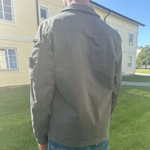 Grå overshirt från Stone Island - Äkta Stone Island-jacka – som ny! Pris: 5 500 kr Plats: Göteborg Säljer en äkta Stone Island-jacka som endast har använts i en vecka – i princip nyskick! Köpt från NK Menswear i Göteborg och kvitto/äkthetslapp med QR-kod finns (se bilder). Modellen är stilren och passar perfekt till både vardag och lite finare tillfällen. Färg: Mörkgrå/olivgrön Storlek: (S) Jackan är självklart 100 % äkta – går att verifiera via certilogo.com med medföljande kod. Nypris i butik: 6500