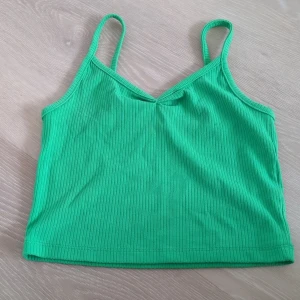Grön ribbad linnetopp - Snygg grön linnetopp med smala axelband och ribbad struktur. Toppen är croppad och har en enkel, stilren design som passar perfekt till jeans eller kjol. Perfekt för varma dagar och somriga outfits.
