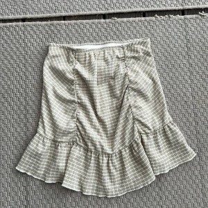 Beige rutig volangkjol S - Supersöt kort kjol i beige och vitt med rutigt mönster och volangkant. Kjolen har en lätt rynkad effekt framtill och är perfekt för dig som gillar en feminin och trendig stil. storlek S från Gina tricot 