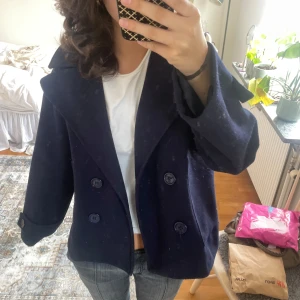 Mörkblå kappa från Design by Si - Säljer en trendig mörkblå kappa från Design by Si. Jackan har dubbelknäppning med stora knappar, bred krage. Perfekt för dig som gillar en tidlös och cool look med lite oversized känsla. En av knapparna på ena armen har lossnat som man kan se på bilden men de går lätt att sy fast eller sätta en säkerhetsnål. Skriv vid frågor😊