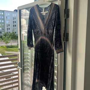 Mönstrad långklänning med v-ringning - Snygg långklänning från H&M med paisleymönster i blått, beige och svart. Klänningen har v-ringning, långa ärmar och plisserad kjol. Materialet är mjukt och följsamt, perfekt för dig som gillar bohemisk stil med coola detaljer. Prislapp finns kvar. Oanvänd.
