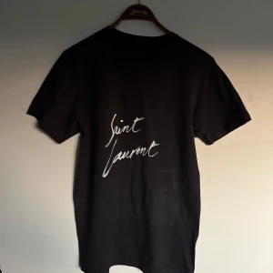 Saint Laurent t shirt - Riktigt fet och eftertraktad Saint Laurent t shirt i mycket bra skick! Är lite osäker på äktheten så därför är priset just nu på 1299kr! nypris runt 4000kr. Storlek S. Tveka inte med att ställa frågor!
